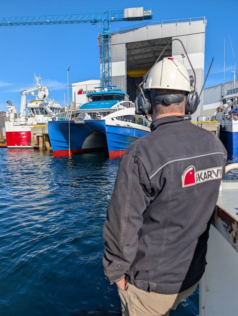 Arbeider med Skarvik-jakke ser mot en catamaran ved kaia på Skarvik